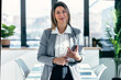 © nenetus - Beautiful elegant business woman working with digital tablet while looking at camera standing in a modern office