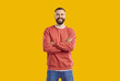 © Studio Romantic - Young smiling bearded man in red sweatshirt and jeans is posing with arms crossed on chest standing isolated on yellow background looking at camera. Sincere human emotions, body language concept.
