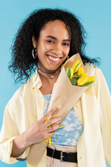 Wall Mural - happy and stylish african american woman holding yellow tulips isolated on blue.