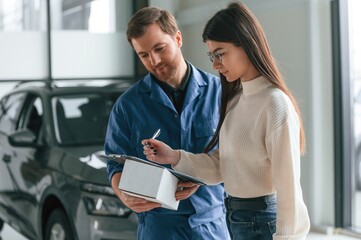 Young woman is visiting auto mechanic in garage. Repair service