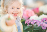 Fototapeta  - Closeup of a little blonde girl in blue shirt holding a flower in one hand with cute expression against the background of hydrangea flowers. Happy childhood