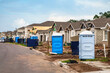 Street view of single-family houses under construction, with dumpsters and portable sanitation units near the curb, in a suburban development in Florida. Digital oil-painting effect.