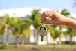 Real estate agent, home keys in female hand on background of house surrounded by palm trees. Buying or rental a villa on ocean coast, holidays or removal to tropical country