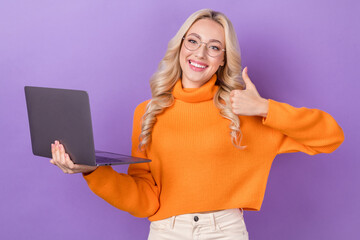 Wall Mural - Photo of positive friendly girl stylish hairdo dressed orange sweater show like good job hold laptop isolated on purple color background