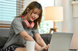 © saltdium - Cute college girl with headphones around her neck Studying online lessons with laptop while sitting on the sofa in house.