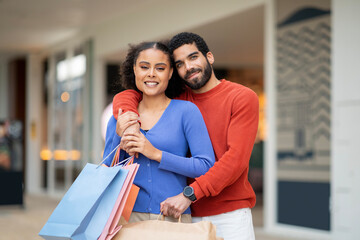 Middle Eastern Couple Embracing Holding Shopping Bags Standing At Mall