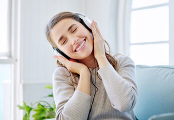 Wall Mural - She loves this song. Cropped shot of an attractive young woman listening to music while relaxing on the sofa at home.