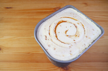 Wall Mural - Tub of Delectable Salted Caramel Macadamia Nut Ice Cream Isolated on Wooden Table