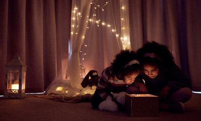 Sticker - Theyre totally enchanted. Shot of two adorable little girls looking at a glowing box in a dark room at home.