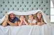 © Delcio/peopleimages.com - Portrait of happy parents with little children lying on bed at home under blanket. Caucasian girls bonding with their mother and father. Smiling young married couple enjoying free time with daughters