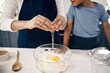 Closeup of female hands cracking a egg into a bowl while baking at home with her son. Woman adding ingredients to a glass bowl on the counter at home while baking with her child