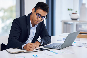 Poster - A focused mind gets more done. Shot of a young businessman writing notes while working on a laptop in an office.
