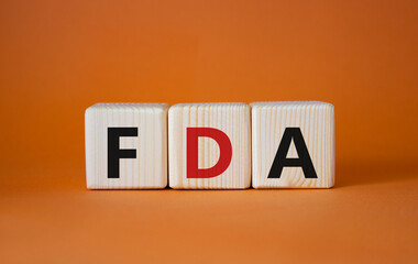 FDA - Food Drug Administration symbol. Wooden cubes with word FDA. Beautiful orange background. Medical and Food Drug Administration concept. Copy space.