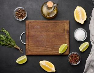 Wall Mural - Various lemon and lime slices on a wooden board. Salt, spices and rosemary branches on a black background, top view