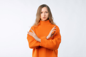 Portrait of woman showing stop gesture with crossed hands, disapprove something, dislike and reject, prohibit action, say no, wearing soft orange sweater, standing over neutral background