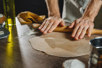 Wall Mural - Unrecognizable man rolling out the dough with a rolling pin on wooden background