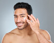 © Beaunitta V W/peopleimages.com - This product is great for acne-prone skin. Shot of a man applying moisturiser to his face while standing against a grey background.