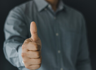 Close up of businessman showing raised thumbs at the camera as a gesture of recommendation or good choice. Professional support and service team demonstrates satisfaction and gives a positive response