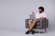 © New Africa - Smiling man with laptop sitting in armchair on light grey background, space for text