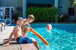 Oudoor summer activity. Concept of fun, health and vacation. Brothers boys eight and five years old with noodle sits near a pool in hot summer day.