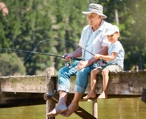 Sticker - A hobby that he will grow up loving. Shot of a little boy fishing with his grandfather at a lake in a forest.