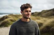© Anne-Marie Albrecht - Environmental portrait photography of a pleased man in his 20s wearing a cozy sweater against a summer landscape or beach background. Generative AI
