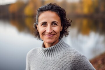 Wall Mural - Portrait of a smiling middle-aged woman in a knitted sweater on a background of a lake