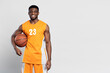 Portrait of confident smiling African American man, professional basketball player holding ball isolated on white background. Sportsman wearing orange basketball uniform looking at camera, copy space