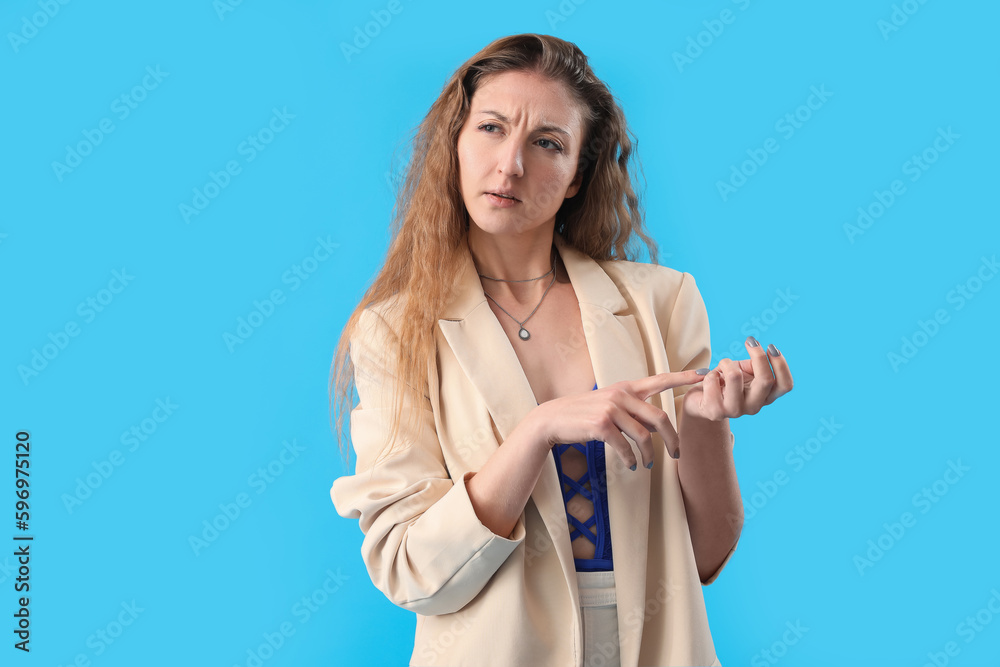 Thoughtful young woman in jacket counting on blue background