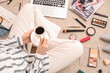 © Pixel-Shot - Woman with cup of coffee, laptop and accessories shopping online on beige carpet, closeup