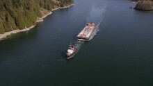 Aerial View Of A Tugboat Pulling A Barge Down A River In The Mountains Near Vancouver, BC On A Bright Summers Day