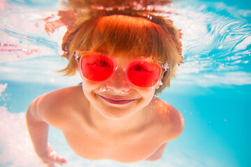 Kid swimming underwater. Summer kids. Happy little boy in swimming pool on summer day. Funny kid swimming and diving in pool. Kid underwater with splashes. Summer children water sports activity.