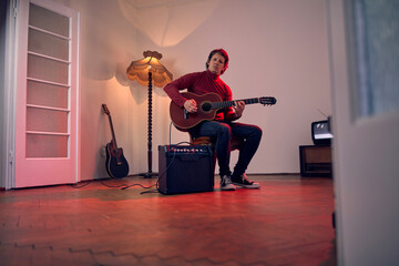 Male musician playing acoustic guitar on the amplifier in retro vintage room.