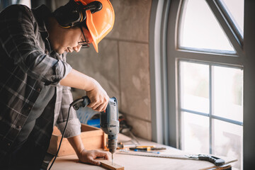 Close up of male mechanic holding electric cordless screwdriver drill with wood screw in the factory. Working with the screw. Professional carpenter.