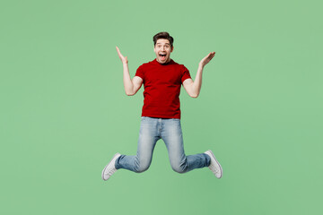 Wall Mural - Full body surprised shocked young brunet man he wear red t-shirt casual clothes jump high spread hands scream yes wow isolated on plain pastel light green background studio portrait Lifestyle concept