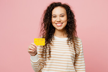 Wall Mural - Young surprised shocked happy fun woman of African American ethnicity she wear light casual clothes hold in hand mock up of credit bank card isolated on plain pastel pink background studio portrait.