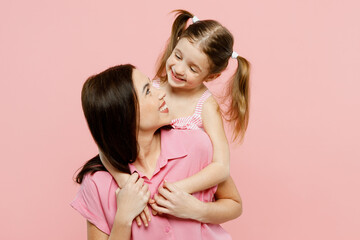 Wall Mural - Happy woman wear casual clothes with child kid girl 6-7 years old. Daughter stand behind mother, look to each other, hug and cuddle isolated on plain pastel pink background. Family parent day concept.