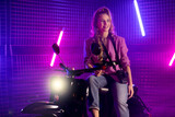 Fototapeta Nowy Jork - 80s style woman on motor scooter with camera in purple studio