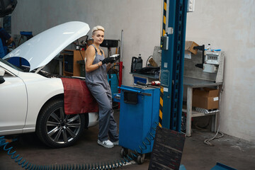 Wall Mural - Young craftswoman stands by a car with a raised hood