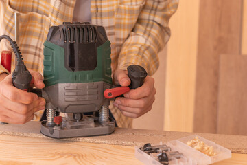 Crop anonymous male carpenter using electric milling machine while cutting wood plank in home workshop