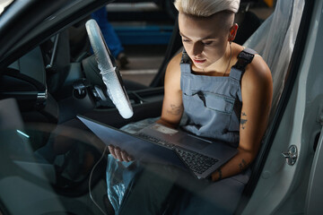 Auto repairwoman conducts computer diagnostics of car with a laptop