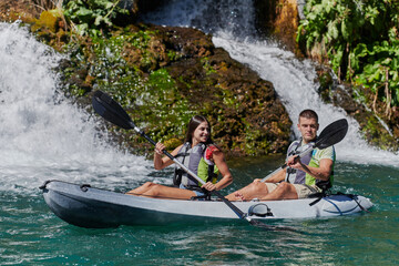 Wall Mural - A young couple enjoying an idyllic kayak ride in the middle of a beautiful river surrounded by forest greenery