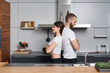 Serious concentrated young couple in the modern kitchen. Standing back to back.