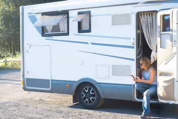 One independent travel woman enjoying vanlife lifestyle sitting outside her motor home camper van using mobile phone with roaming connection. Wanderlust and adventure journey trip concept people life