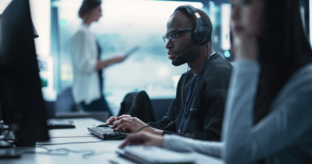 Poster - Portrait of a Smart African Young Specialist Working in a Technological Startup Help Desk Department, Using Computer in a Diverse Office. Black Man Wearing Glasses and Headphones with a Microphone