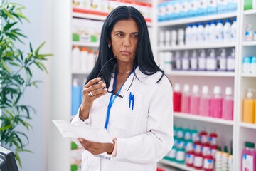 Wall Mural - Middle age hispanic woman pharmacist reading prescription at pharmacy