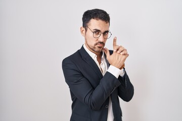 Sticker - Handsome business hispanic man standing over white background holding symbolic gun with hand gesture, playing killing shooting weapons, angry face