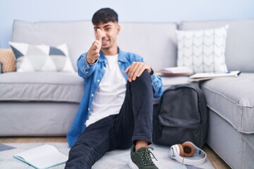 Wall Mural - Young hispanic man sitting on the floor studying for university smiling friendly offering handshake as greeting and welcoming. successful business.