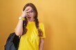 © Krakenimages.com - Young caucasian woman wearing student backpack over yellow background peeking in shock covering face and eyes with hand, looking through fingers with embarrassed expression.