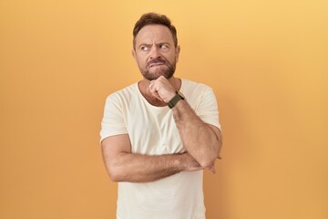 Sticker - Middle age man with beard standing over yellow background thinking worried about a question, concerned and nervous with hand on chin